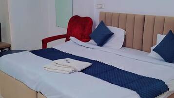 Uma cama bem arrumada com cabeceira, uma cadeira vermelha e uma parede branca com interruptor de luz.