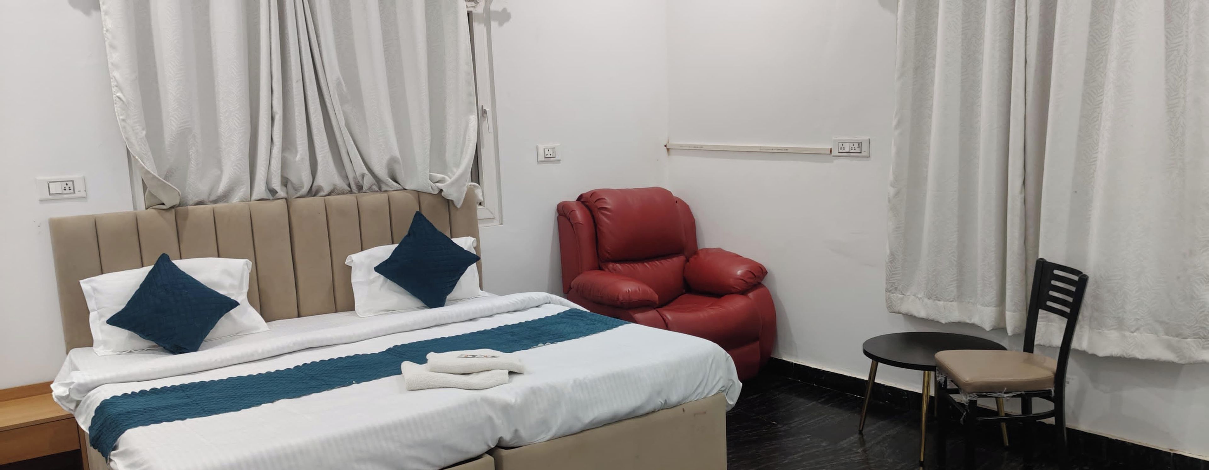 Una habitación de hotel con una cama, un sillón de cuero rojo, una mesita y una silla.