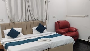 Una habitación de hotel con una cama, un sillón de cuero rojo, una mesita y una silla.