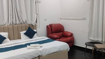 Una habitación de hotel con una cama, un sillón de cuero rojo, una mesita y una silla.