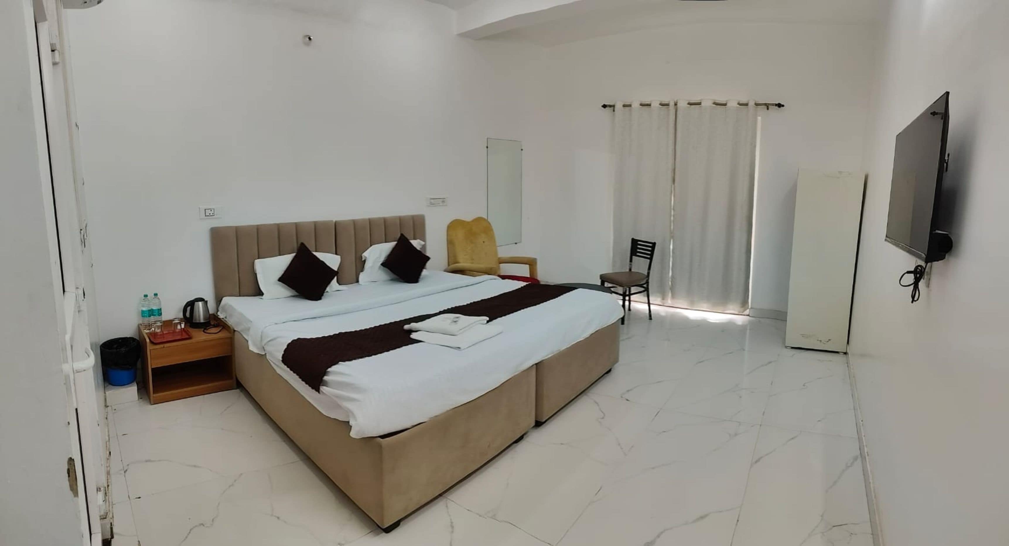 Une chambre d’hôtel avec un grand lit, une télévision, une chaise et un bureau avec une lampe.