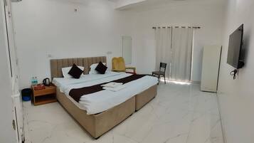 Quarto de hotel com cama grande, televisão, cadeira e escrivaninha com abajur.