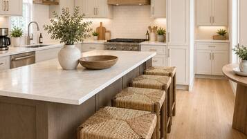 A modern kitchen with a central island, wooden stools, and pendant lighting.