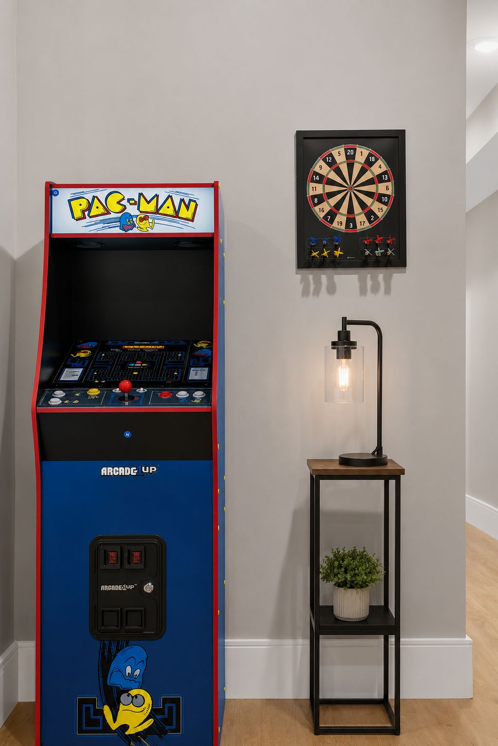 Una máquina arcade de Pac-Man, un dardo y una mesa con una lámpara y una planta.