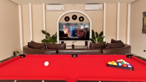 A pool table with a cue ball and a set of billiard balls, a brown leather sofa with cushions, and a television mounted on the wall. - Beautiful Private Pool Villa – Perfect Pattaya Escape (Pattaya City)