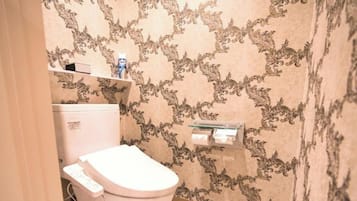Une salle de bain avec des toilettes, une étagère au-dessus des toilettes et un mur décoré d’un motif.