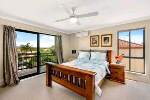 Een slaapkamer met een bed, nachtkastje, plafondventilator en een groot raam.