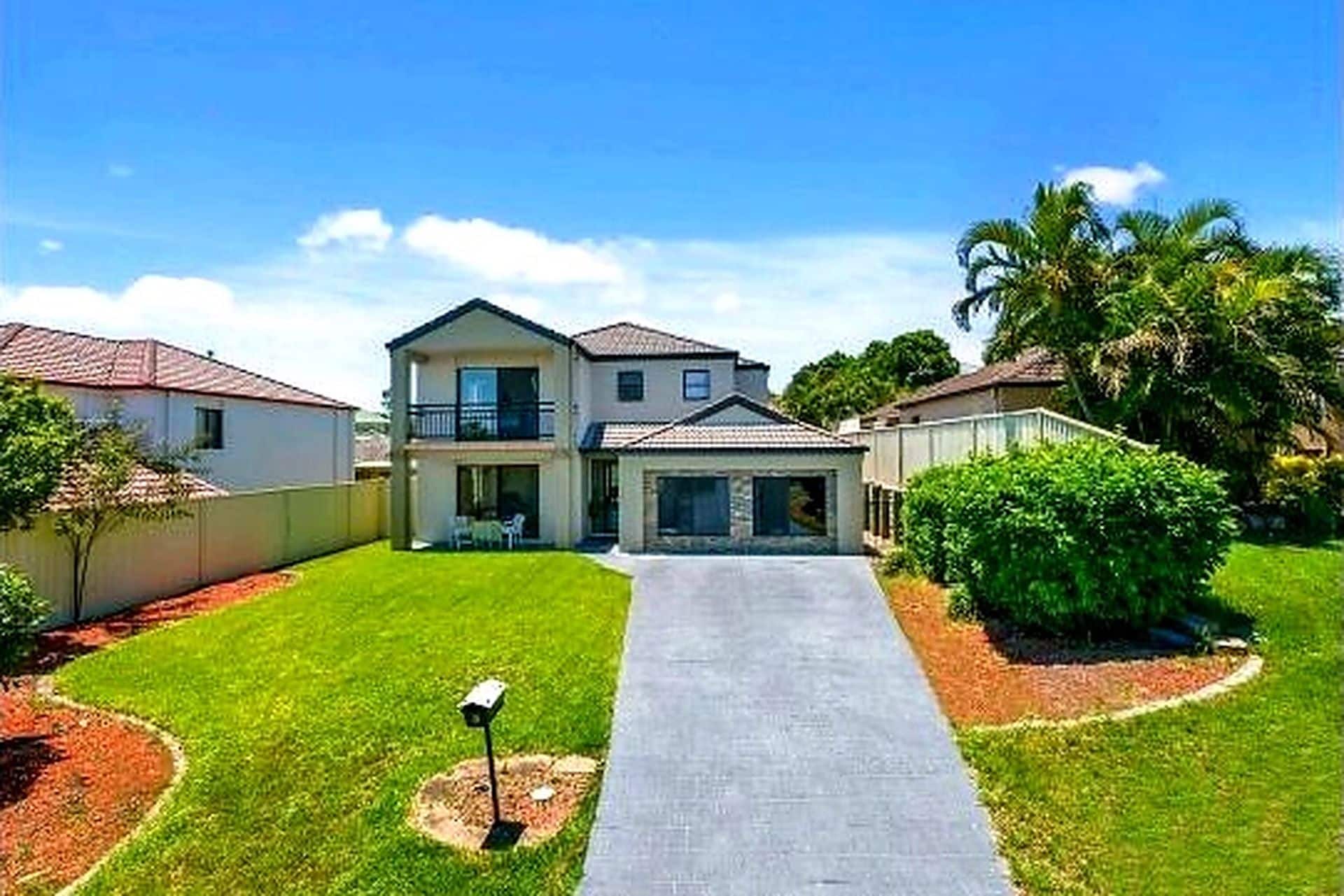 A two-story residential house with a front driveway, a balcony, and a well-maintained lawn.
