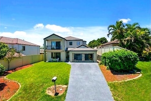 A two-story residential house with a front driveway, a balcony, and a well-maintained lawn. - Room-happy House for Happy Guests (Gold Coast)