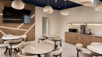 A modern interior with round tables and chairs, a kitchen area with a coffee machine, and pendant lighting.