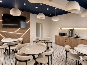A modern interior with round tables and chairs, a kitchen area with a coffee machine, and pendant lighting. - Azimut Hostel (Almaty)
