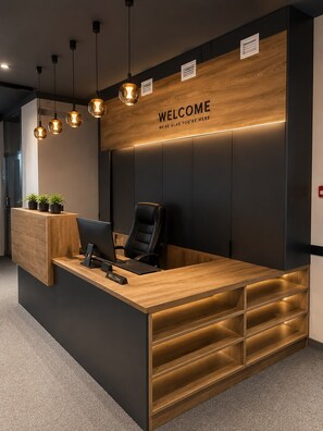 A reception desk with a 'WELCOME' sign, a computer, a chair, and potted plants. - Azimut Hostel (Almaty)