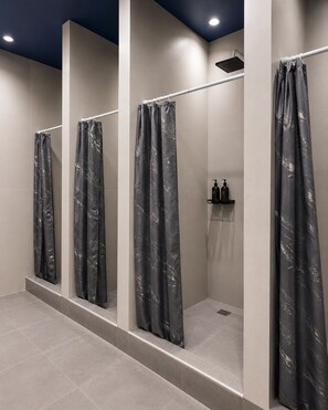 A modern bathroom with three shower stalls, each with a marble-patterned curtain. - Azimut Hostel (Almaty)