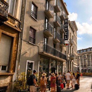A hotel with a sign, multiple balconies, and a group of people with luggage. - Brxxl5 City Centre Hostel (Brussels)