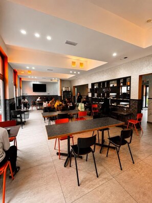 A modern dining area with tables and chairs, a flat-screen TV mounted on the wall, and a counter with a sign reading 'BEXL5'. - Brxxl5 City Centre Hostel (Brussels)