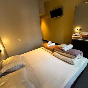 A hotel room with a bed, pillows, a flat-screen TV mounted on the wall, and a nightstand with a lamp. - Brxxl5 City Centre Hostel (Brussels)