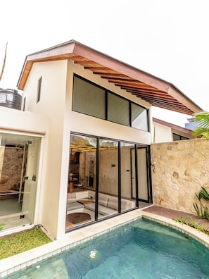 Une maison moderne à deux étages, dotée d’une piscine, de grandes baies vitrées et d’un mur en pierre.