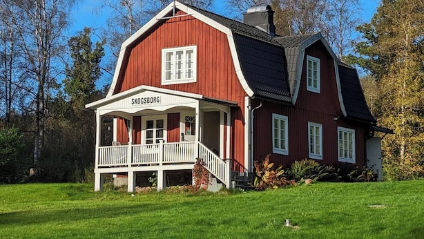 Una casa de madera roja con un porche blanco y un letrero que dice 'SKOGSBORG'.