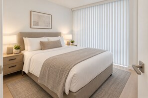 Ein modernes Schlafzimmer mit einem Bett, Nachttischen, einem Fenster mit Jalousien und einem gerahmten Bild.