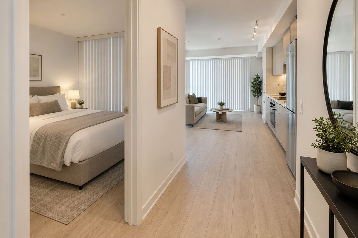 Ein modernes Hotelzimmer mit Bett, Nachttisch, Lampe und Blick auf den Flur.