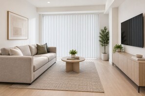 Ein modernes Wohnzimmer mit einer Couch, einem Couchtisch, einem Fernseher und einem großen Fenster mit Jalousien.
