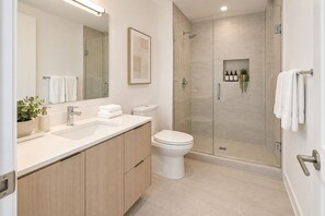 Ein modernes Badezimmer mit einer Duschkabine, einem weißen Waschbecken mit Spiegel und einer Toilette.