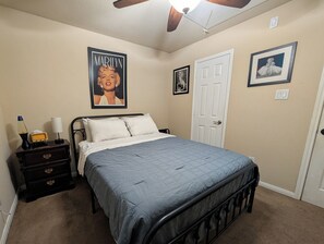 A bedroom with a bed, a nightstand with a lamp, a poster on the wall, and a door. - Private World for two, one bedroom house with music & arcade games. (Houston)