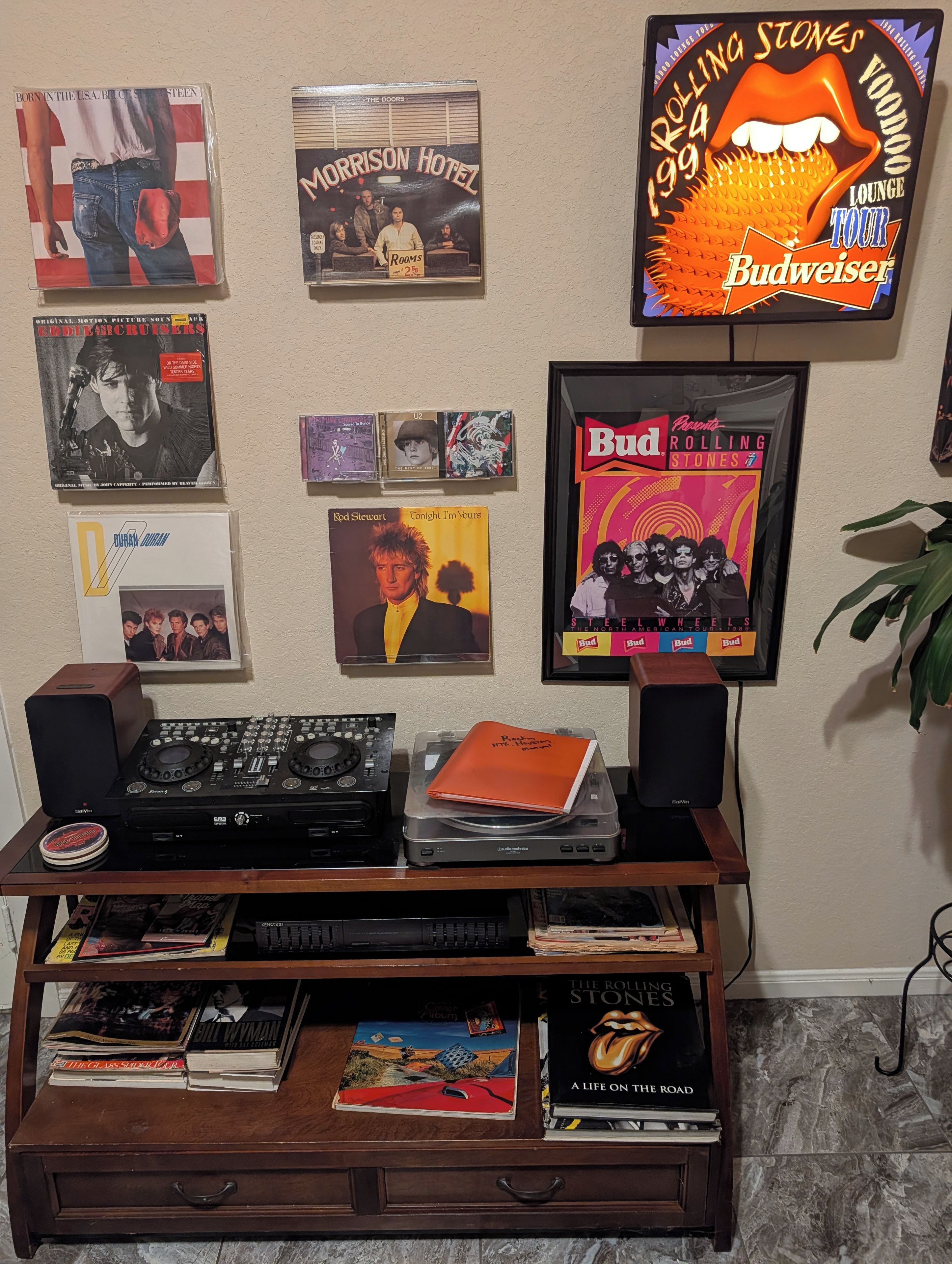 A wall with framed music album covers, a DJ setup, and a bookshelf with books.