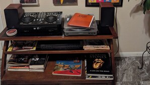 Una pared decorada con portadas de discos, un equipo de DJ y una estantería con libros.