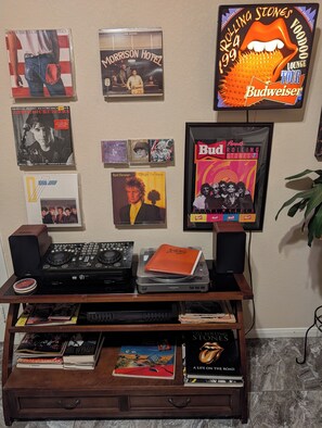 A wall with framed music album covers, a DJ setup, and a bookshelf with books. - Private World for two, one bedroom house with music & arcade games. (Houston)
