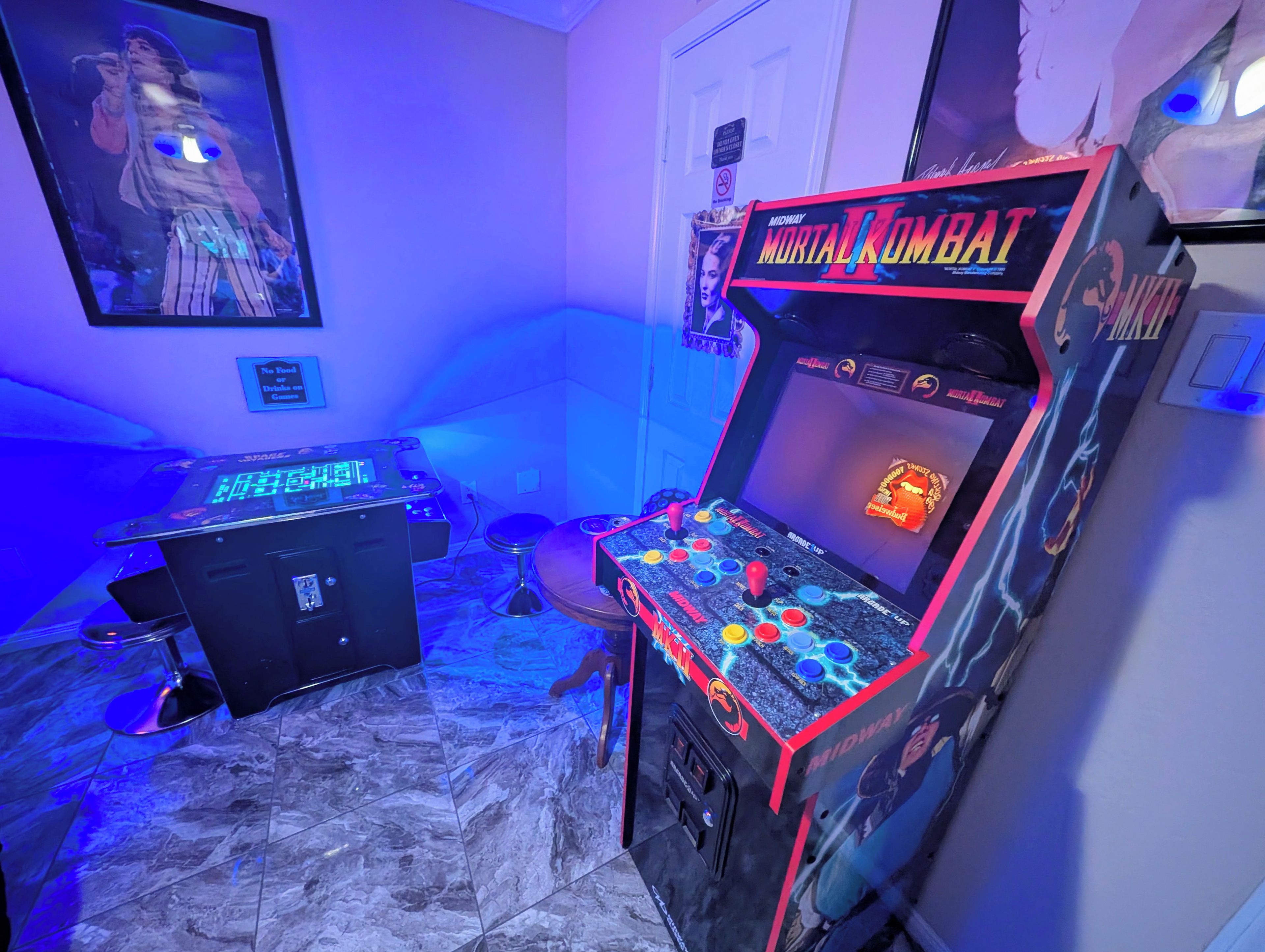 Habitación con máquinas recreativas, incluyendo un juego de Mortal Kombat, y un cartel que prohíbe comer y beber en la pared.
