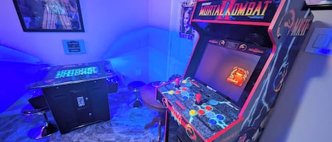 Habitación con máquinas recreativas, incluyendo un juego de Mortal Kombat, y un cartel que prohíbe comer y beber en la pared.