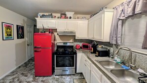 Una cocina compacta con armarios blancos, un refrigerador rojo, una estufa y un lavamanos.