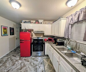 A compact kitchen with white cabinets, a red refrigerator, a stove, and a sink. - Private World for two, one bedroom house with music & arcade games. (Houston)