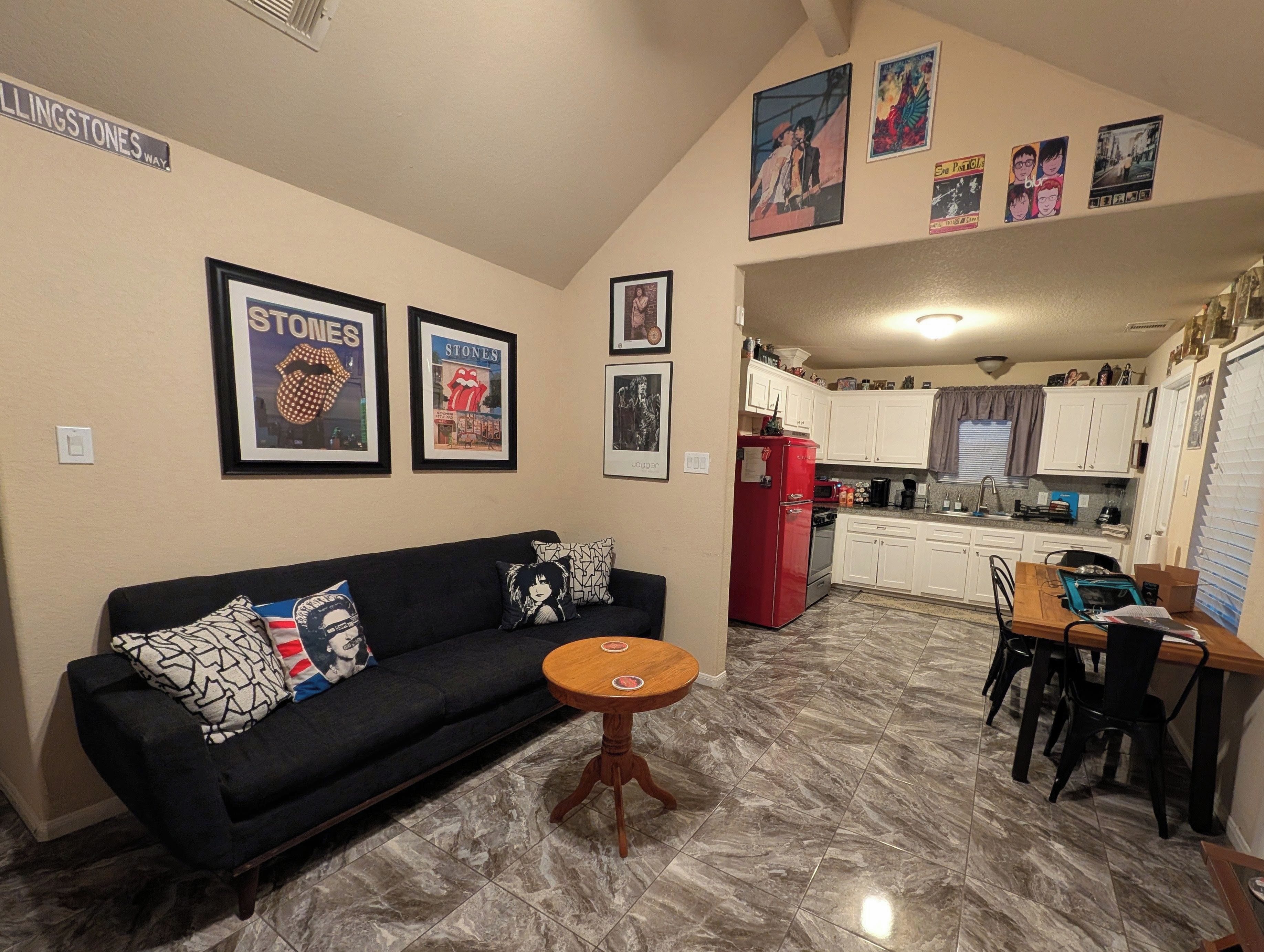 Un espacio habitable compacto con sofá, una pequeña mesa redonda y una zona de cocina con armarios blancos y un refrigerador rojo.