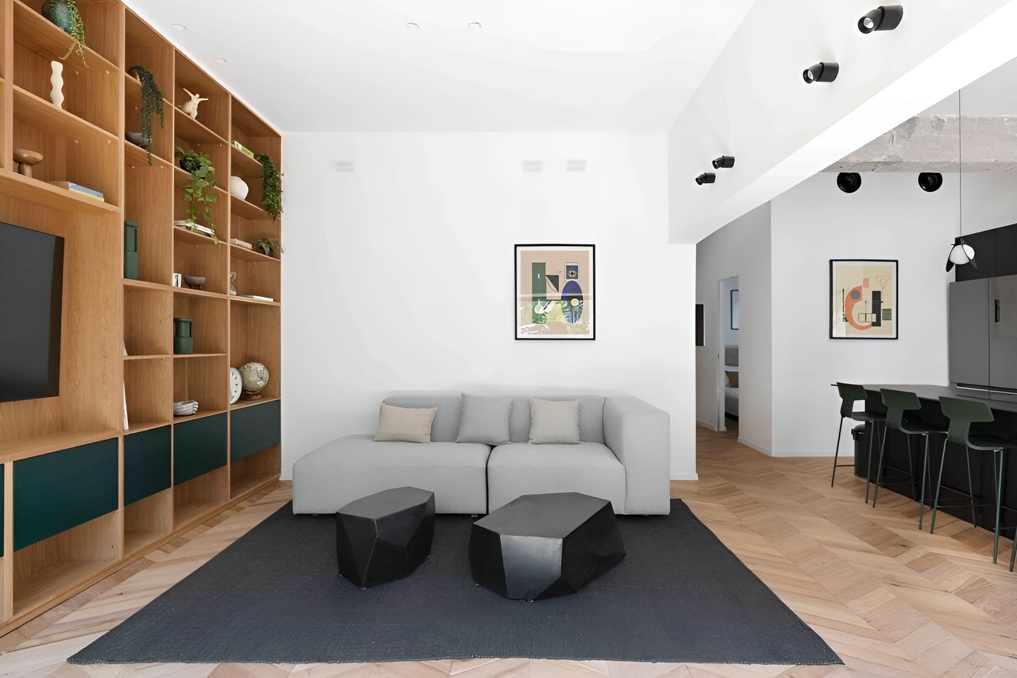 A modern living room with a sofa, two black ottomans, a wooden bookshelf, and a flat-screen TV.