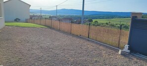 A gravel driveway leading to a fenced property with a view of distant hills and houses.