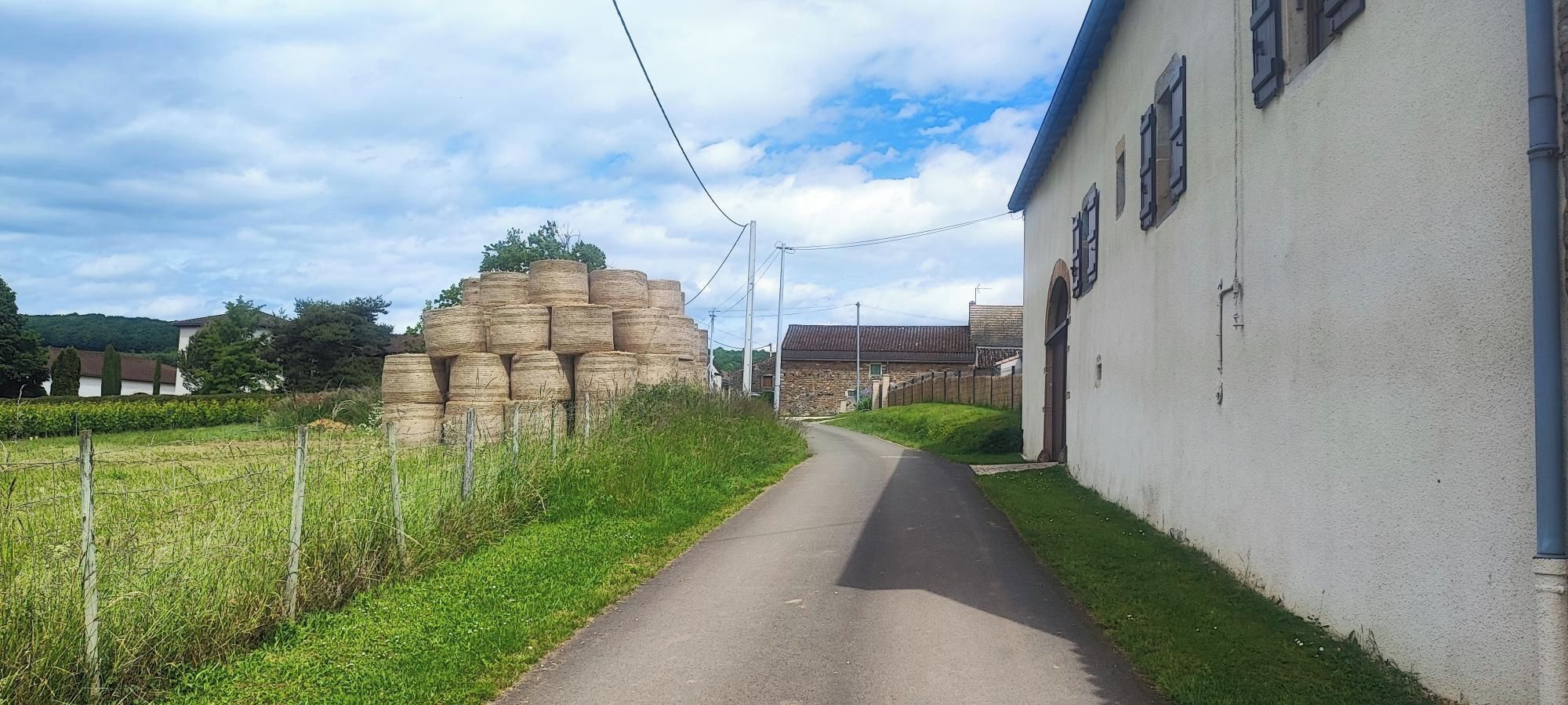 Une route de campagne bordée d’un bâtiment blanc et de bottes de foin.
