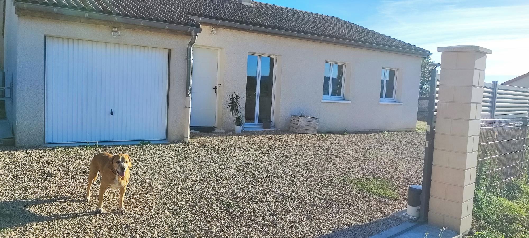 Un bâtiment d’un seul étage, doté d’une porte de garage, d’un petit porche agrémenté d’un pot de fleurs et d’une allée gravillonnée.