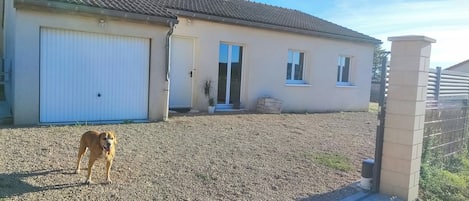 A single-story building with a garage door, a small porch with a potted plant, and a gravel driveway.