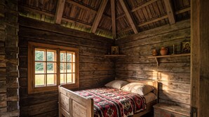 Une pièce rustique en bois, avec un lit, une fenêtre et des étagères ornées d’icônes religieuses.