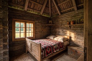 A rustic wooden room with a bed, a window, and shelves with religious icons.