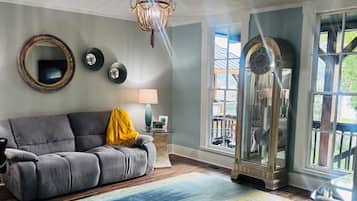 A living room with a grey sofa, a patterned rug, a chandelier, and a large window with a view.