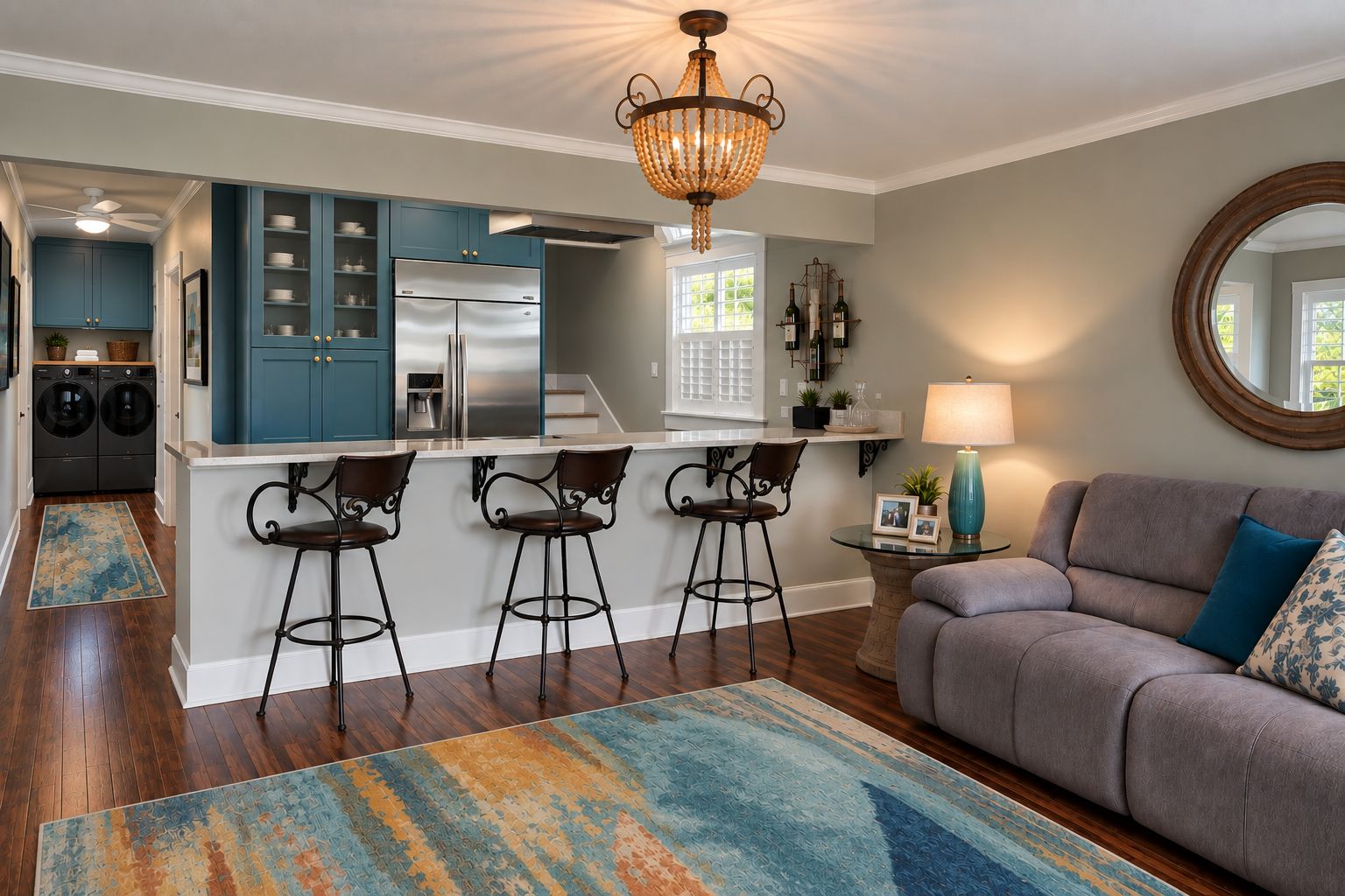 A modern kitchen with a central island, bar stools, a dining area with a round table, and a living room with a sofa and a round mirror.