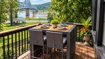 A balcony with wicker furniture, a view of a river, and a bridge in the background.