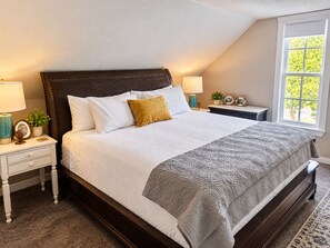 Un dormitorio con una cama grande, dos mesitas de noche, una ventana y vistas a zonas verdes.