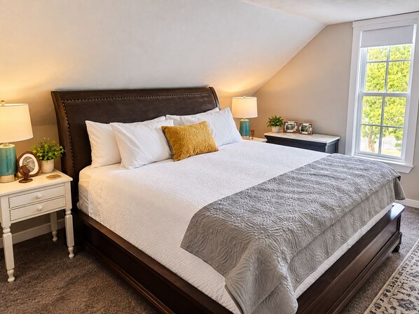 A bedroom with a large bed, two bedside tables, a window, and a view of greenery outside.