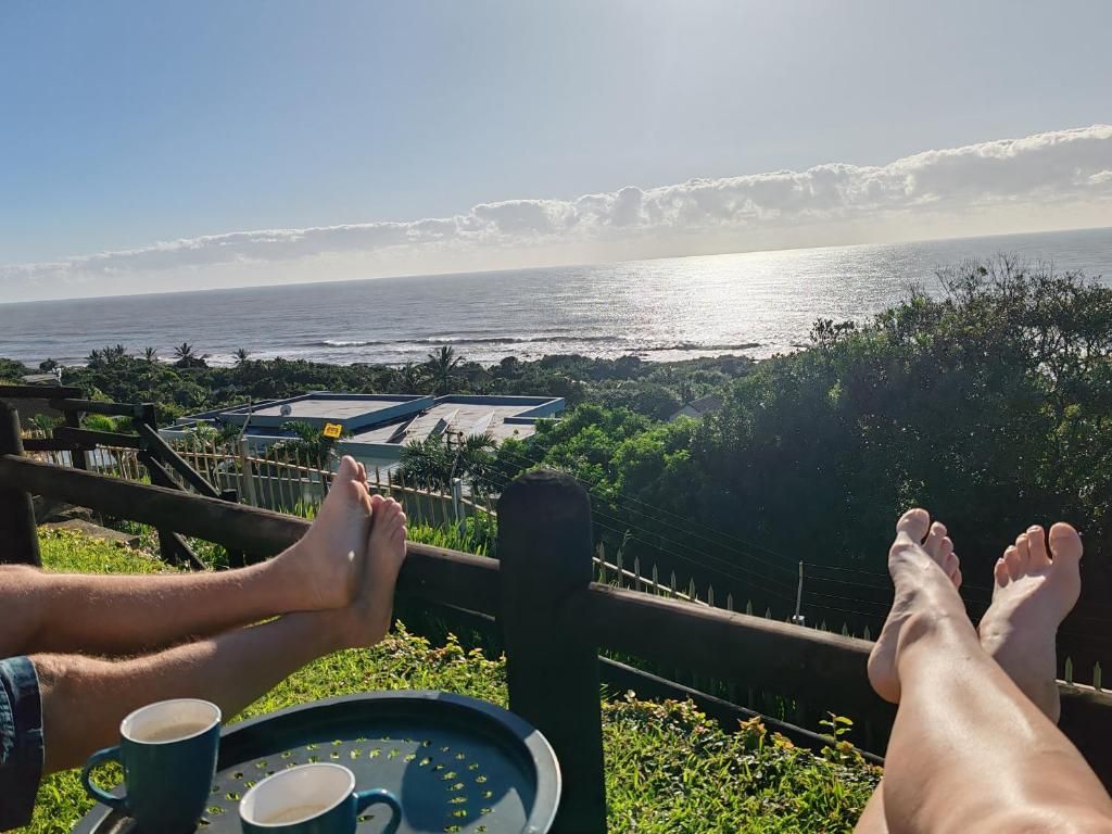 A person relaxing with feet propped up on a railing overlooking a coastal view.