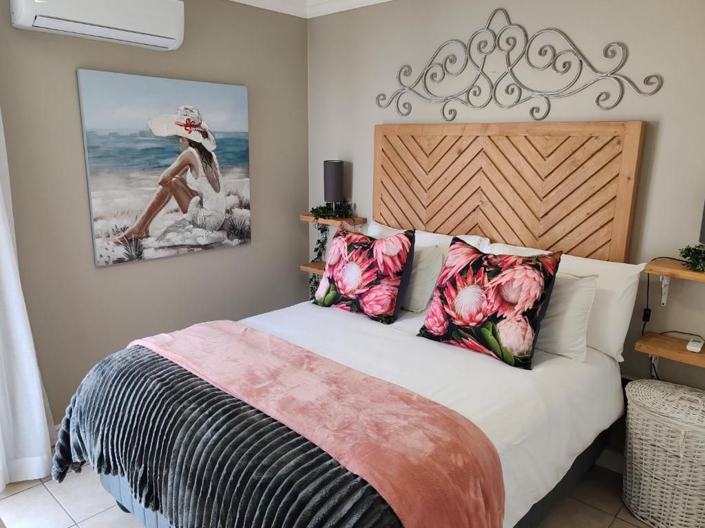 A bedroom with a bed, a headboard, a painting, and a decorative wall piece.
