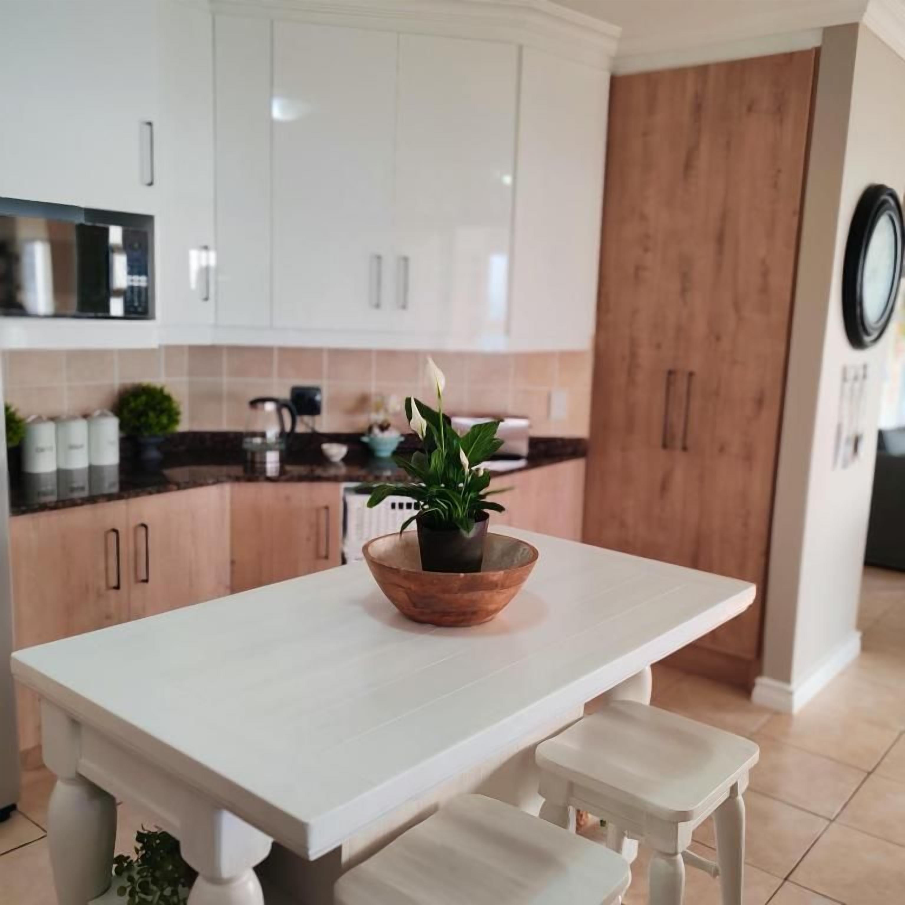 Eine moderne Küche mit weißen Schränken, einer Holzvertäfelung, einem weißen Esstisch mit Bänken und einem Topf mit Pflanze auf dem Tisch.